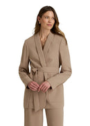 Woman wearing a beige suit with a belt on a plain background