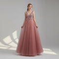 Pink evening gown with beaded top on a model against a white curtain background