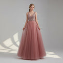 Pink evening gown with beaded top on a model against a white curtain background