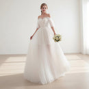 Woman in a white wedding dress holding flowers in a bright room with white curtains.